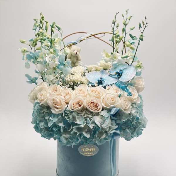 Blue and white floral arrangement in a round hatbox with a small teddy bear