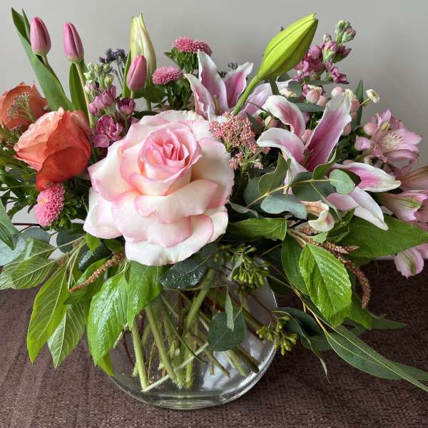 Mixed bouquet of pink roses, lilies, and tulips in a glass vase