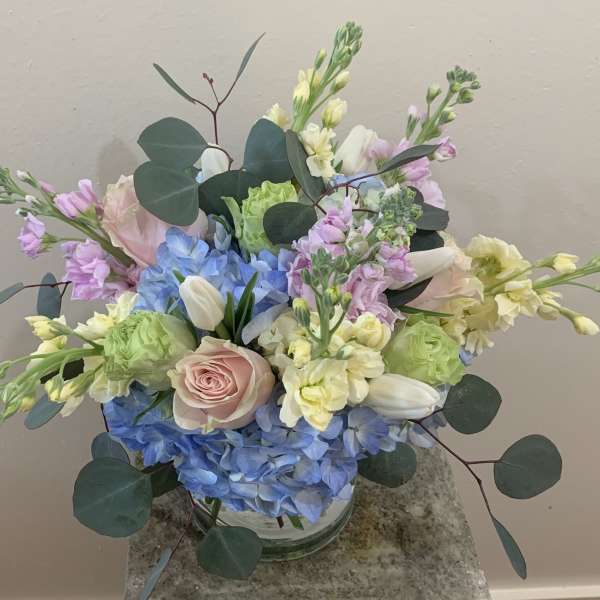 Pastel bouquet with blue hydrangeas, pink roses, and white tulips in a glass vase