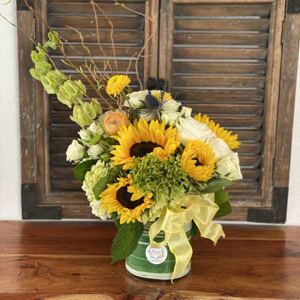 Sunflower and white rose arrangement in a striped tin container with a yellow ribbon