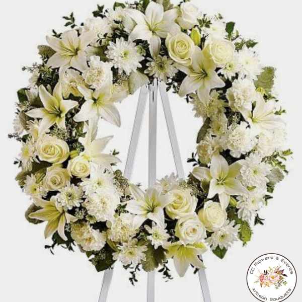 Large white funeral wreath with lilies and roses displayed on a white easel stand