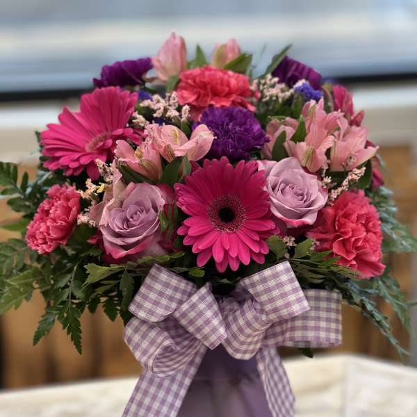 Pink and purple mixed bouquet in a lavender vase with a plaid ribbon