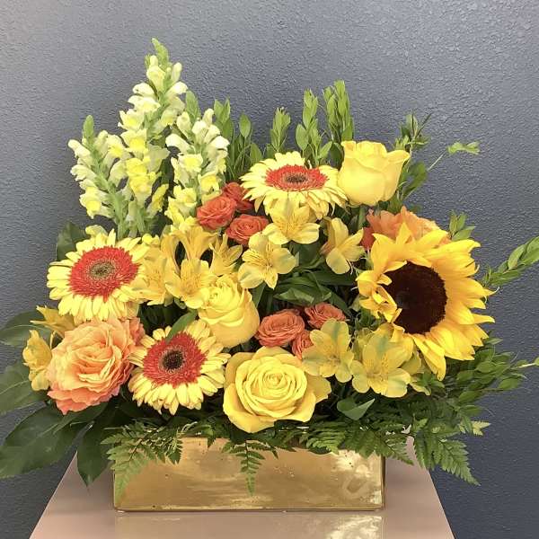 Yellow and orange mixed flower arrangement in a gold rectangular vase