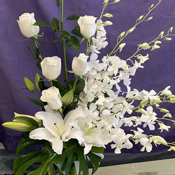 White roses, lilies, and orchids arranged in a tall vase