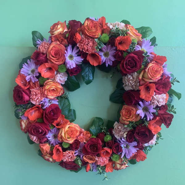 Circular floral wreath with roses, daisies, and carnations on a green background