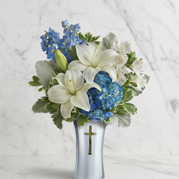White lilies and blue flowers in a silver vase with a cross
