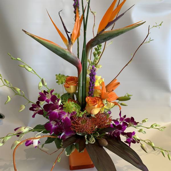 Tropical floral arrangement with orange birds of paradise and purple orchids in a vase