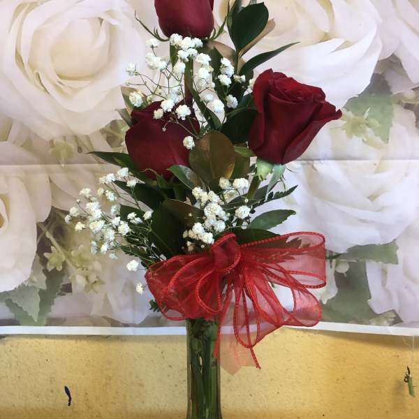 Three red roses in a glass vase with baby's breath and a red ribbon