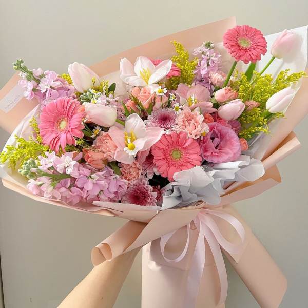 Pink mixed bouquet with gerbera daisies, tulips, and lilies wrapped in pastel paper