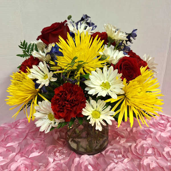 Bouquet of red roses, yellow spider mums, and white daisies in a glass vase