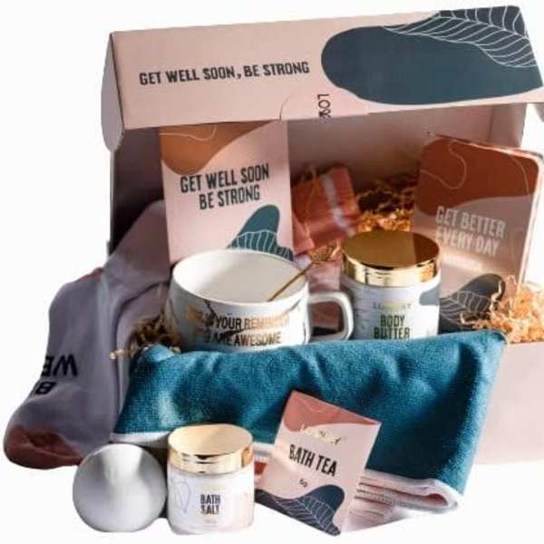 Get well gift box with mug, body products, towel, socks, and bath items arranged in pink packaging.