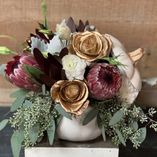 Floral arrangement in a white pumpkin-shaped vase with pink, white, and gold blooms