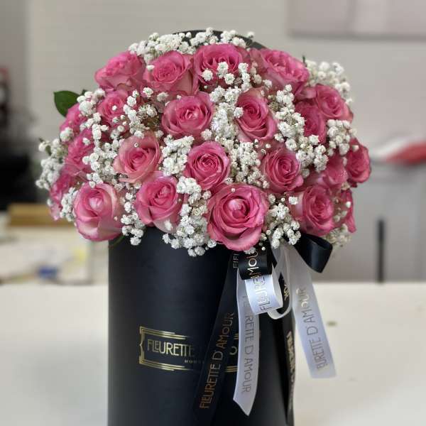 Pink roses arranged in a black hatbox with white baby's breath
