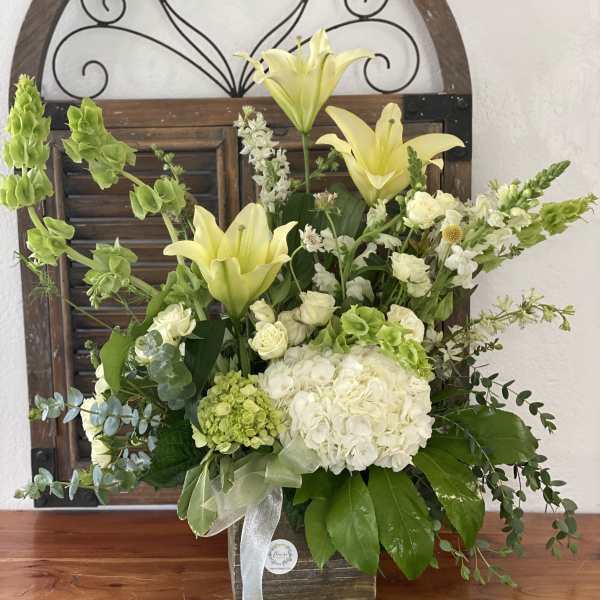 White and green floral arrangement with lilies and roses in a wooden container