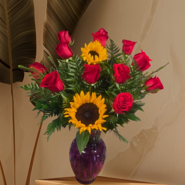 Red roses and sunflowers arranged in a purple glass vase