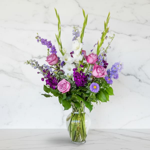 Mixed bouquet of pink roses, white blooms, and purple flowers in a glass vase