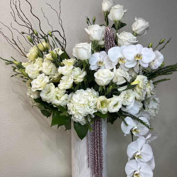 White roses and orchids arranged in a tall white vase