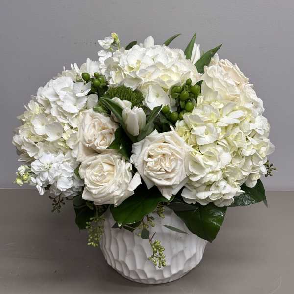 Low white arrangement of roses and hydrangeas in a textured white vase