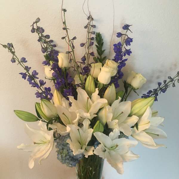 White lilies and purple delphinium in a glass vase