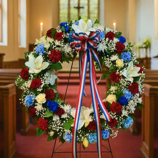 Floral wreath with red, white, and blue flowers on a stand in a church