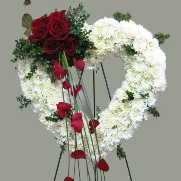 Heart-shaped floral wreath with red roses and white flowers on a stand