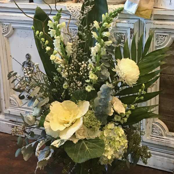 Tall floral arrangement with pale yellow blooms in a glass vase