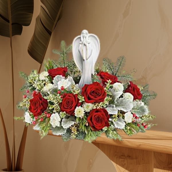 Red roses and white flowers arranged around a white angel figurine