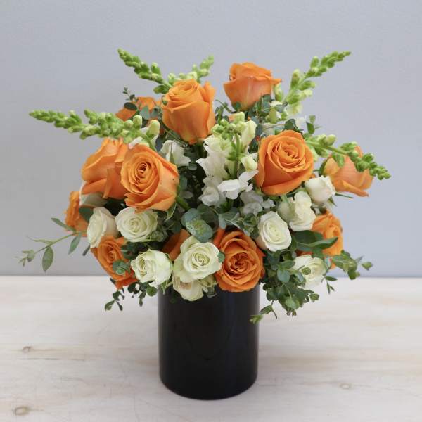 Orange and cream roses with white snapdragons in a black cylinder vase