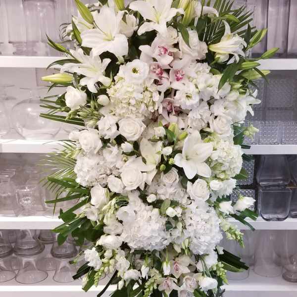 Large white funeral spray with lilies, roses, and orchids on a standing easel