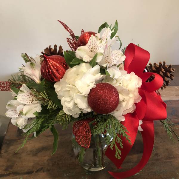 Holiday bouquet of white flowers with red ornaments and ribbon in a glass vase