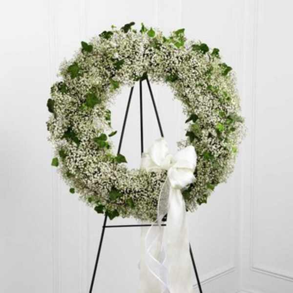 White floral wreath on a black stand with a white ribbon bow