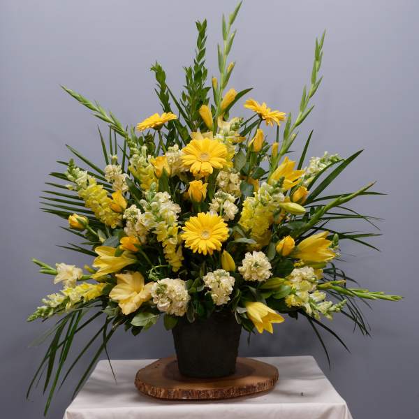 Yellow floral arrangement in a black pot with tall greenery