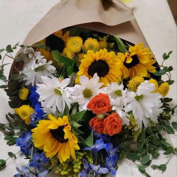 Bouquet of sunflowers, white daisies, and orange roses wrapped in brown paper