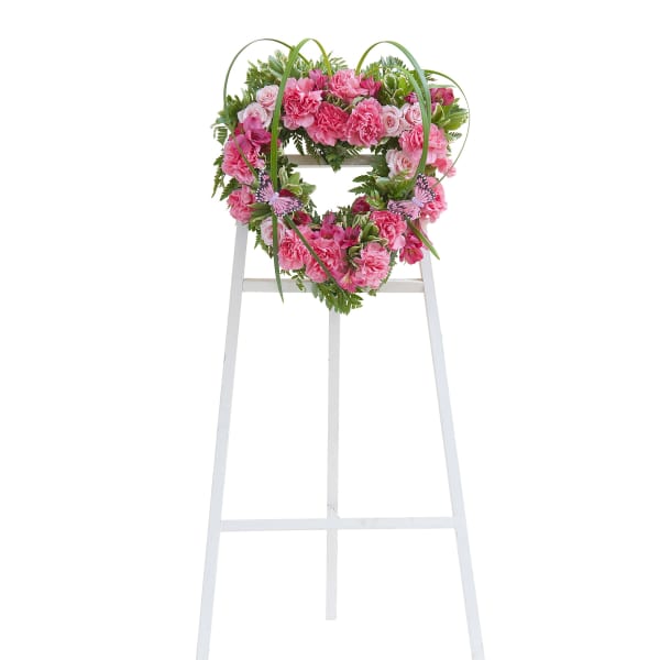 Heart-shaped wreath of pink flowers on a white easel stand