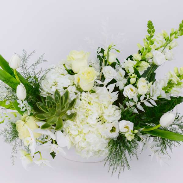 White floral arrangement with tulips, roses, and orchids in a low container