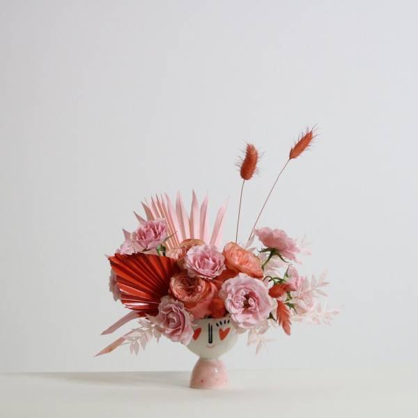 Pink floral arrangement in a face-painted ceramic vase with orange accents