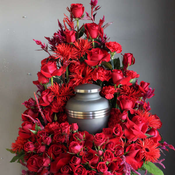 Red rose funeral arrangement around a gray urn