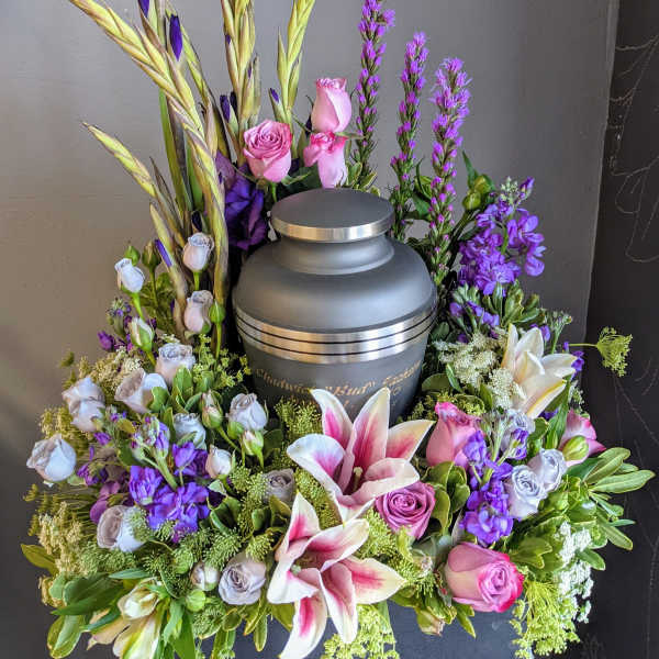 Floral urn arrangement with pink lilies and roses around a gray cremation urn