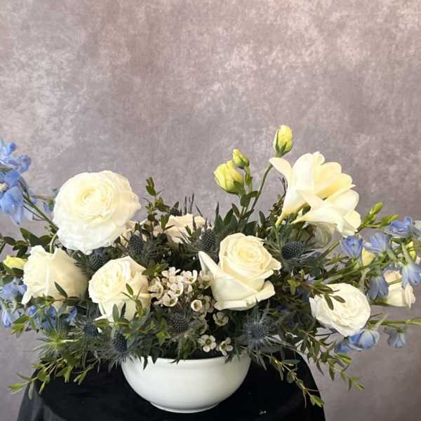 White roses and blue flowers arranged in a white bowl vase