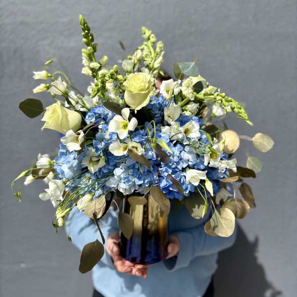 Blue hydrangea bouquet with white roses and snapdragons in a glass vase