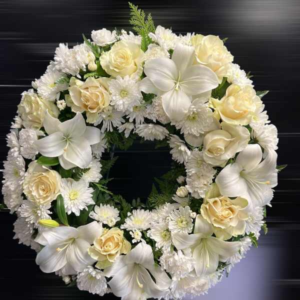 Round wreath of white lilies, cream roses, and white chrysanthemums on a dark background