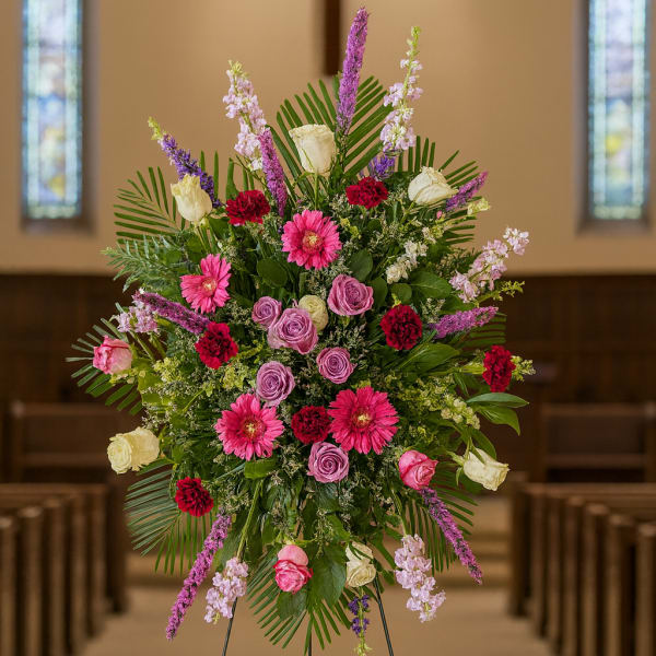 Tall floral spray with pink, purple, and white flowers on an easel in a church