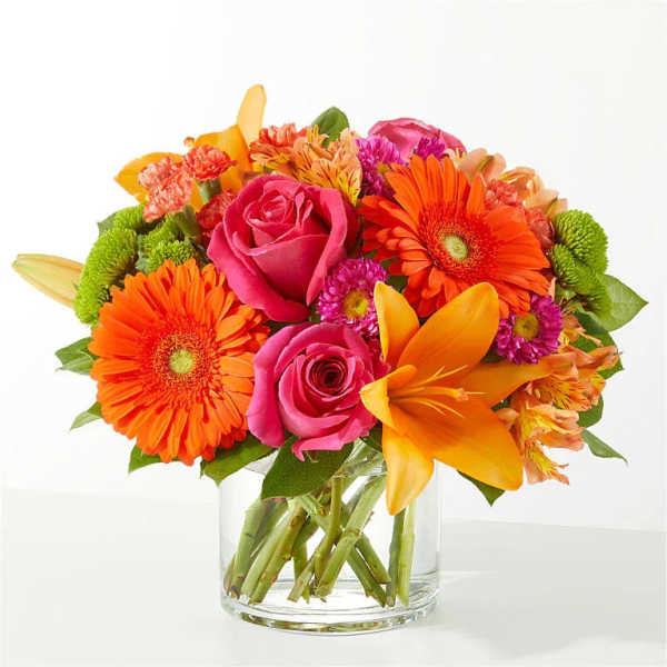 Bright mixed bouquet of roses, gerbera daisies, lilies, and mums in a glass vase