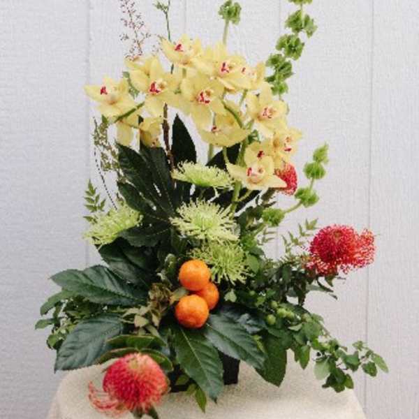 Tall floral arrangement with yellow orchids and red blooms in a container