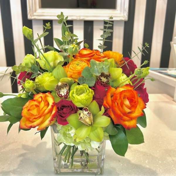 Bright mixed bouquet of roses and green orchids in a clear glass vase