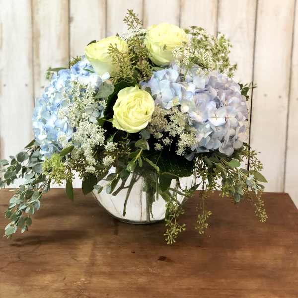 Blue and lavender hydrangeas with pale yellow roses in a glass vase