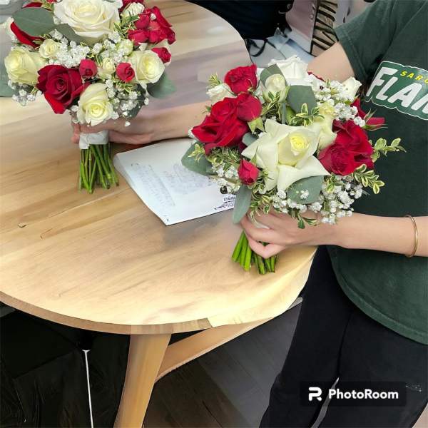 Two hand-held bouquets of red and white roses on a table
