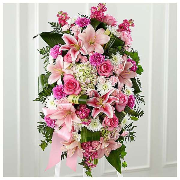 Standing spray of pink lilies, roses, carnations, and white daisies with pink ribbon on an easel