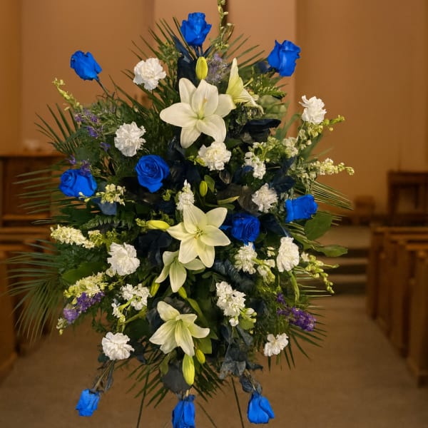 Standing floral spray with blue roses and white lilies on an easel