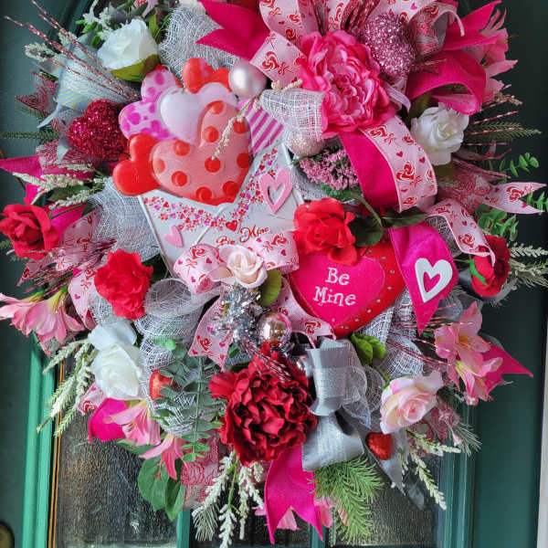 Heart-themed wreath with pink and red flowers, ribbons, and a "Be Mine" sign